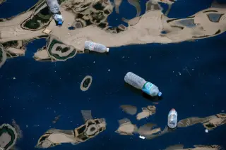 Illustration: Discarded plastic bottles float on dark water with distorted building reflections.