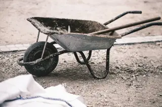 Illustration: An empty, worn wheelbarrow resting on a gravel construction area with a wooden handle inside.